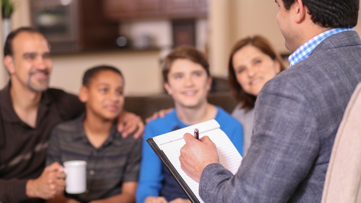 A behavior analyst takes notes while casually speaking to a family of four