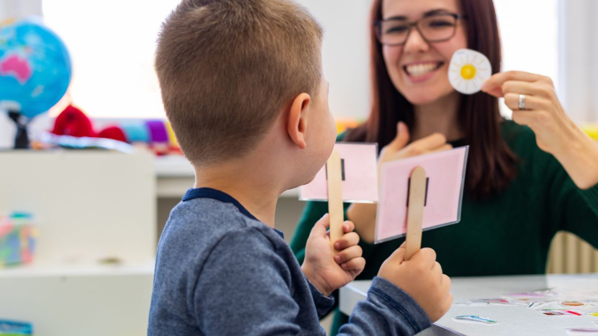 A behavior therapist uses visual aids (daisy) to help teach a child holding flashcards on sticks